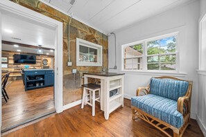 A room with a stone accent wall, a wooden floor, a wicker sofa, a small white table, and a television in the background.