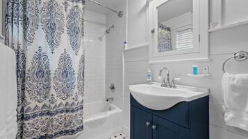 Une salle de bain avec un rideau de douche, un lavabo, un miroir et un porte-serviettes.