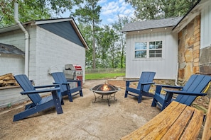 An outdoor seating area with Adirondack chairs and a fire pit, surrounded by a stone and wooden building.