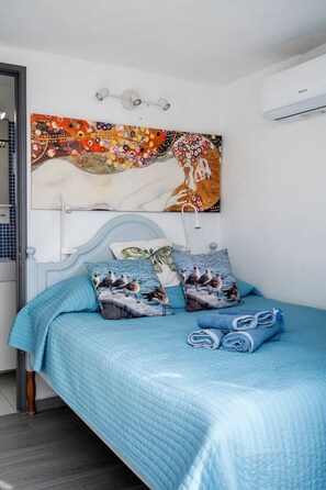 Ein Schlafzimmer mit einem Bett, Kissen, einer Wandklimaanlage und einem Gemälde.