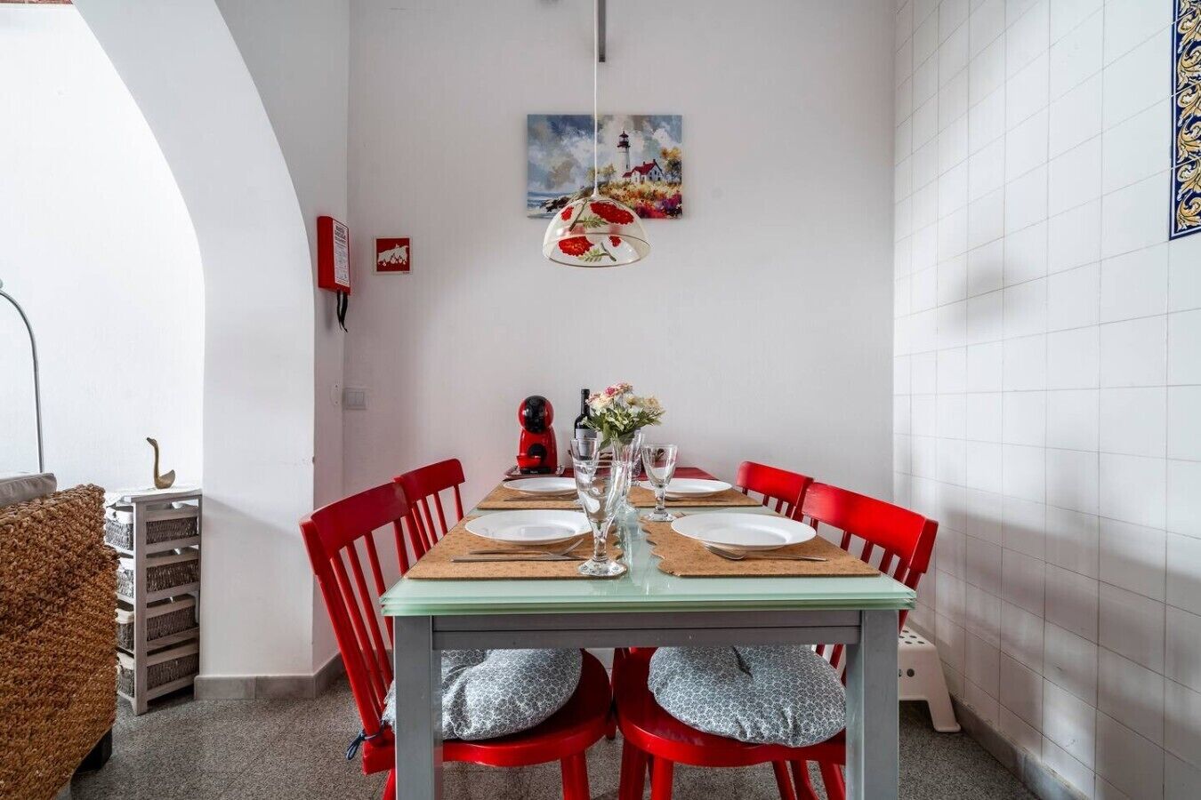 Een eetgedeelte met een tafel gedekt voor twee personen, rode stoelen, een hanglamp en een schilderij aan de muur.