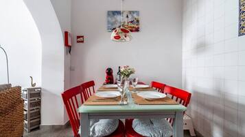 Een eetgedeelte met een tafel gedekt voor twee personen, rode stoelen, een hanglamp en een schilderij aan de muur.