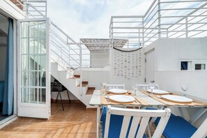 A dining area with a table set for four, a staircase, and a view of the sky. - Casa Teresa — city house with sea view (Olhão)