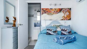 A bedroom with a bed, pillows, a dresser, a mirror, and a wall-mounted artwork.