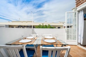 An outdoor dining area with a table set for two, white chairs, and a view of buildings and greenery in the background. - Casa Teresa — city house with sea view (Olhão)