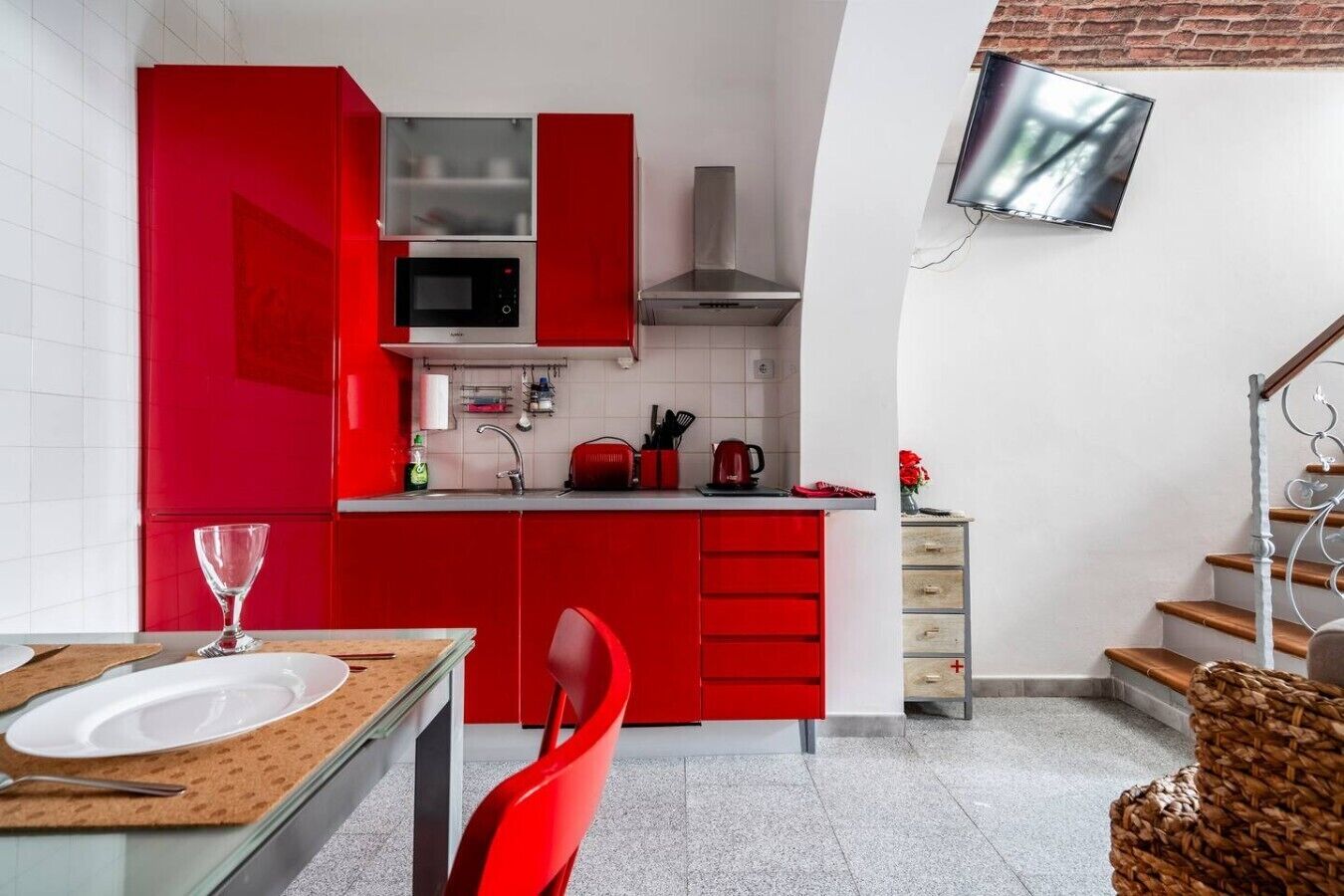 A compact kitchen with red cabinetry, a microwave, and a stainless steel range hood.