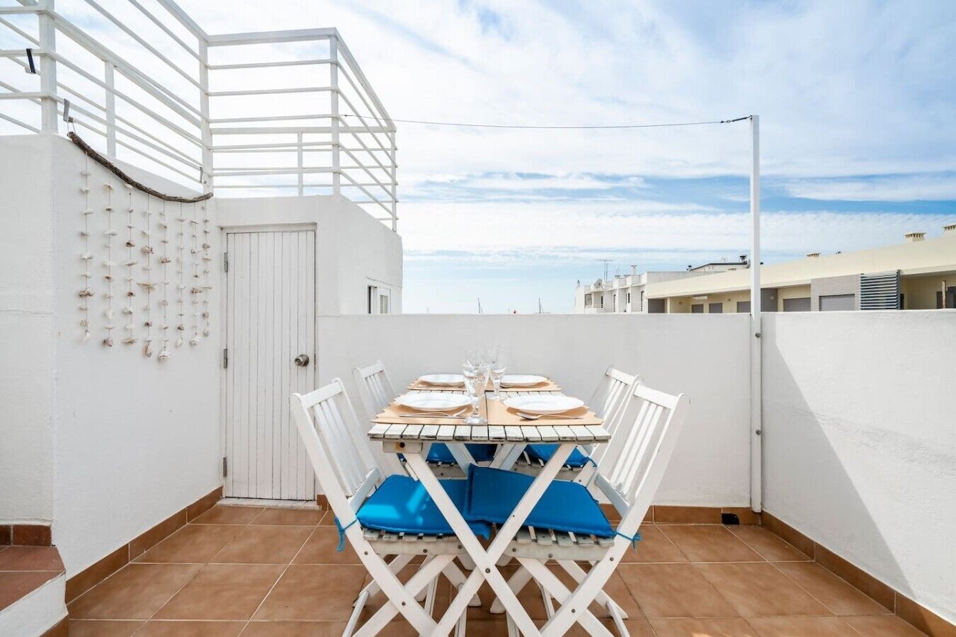 Una terraza en la azotea con una mesa preparada para cuatro personas, sillas blancas y vistas del horizonte de la ciudad.