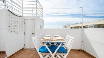 Una terraza en la azotea con una mesa preparada para cuatro personas, sillas blancas y vistas del horizonte de la ciudad.