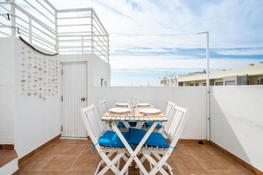 Una terraza en la azotea con una mesa preparada para cuatro personas, sillas blancas y vistas del horizonte de la ciudad.