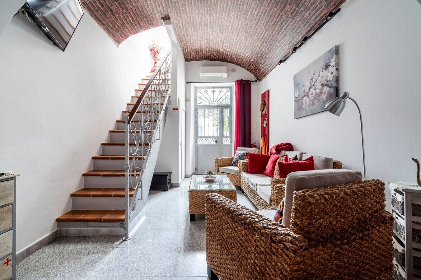 Una escalera que lleva a una puerta, una sala de estar con muebles de mimbre y un cuadro en la pared.