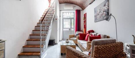 A staircase leading to a door, a living room with wicker furniture, and a painting on the wall.