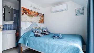 Un dormitorio con cama, almohadas, un cuadro, aire acondicionado y un baño visible a través de una puerta abierta.