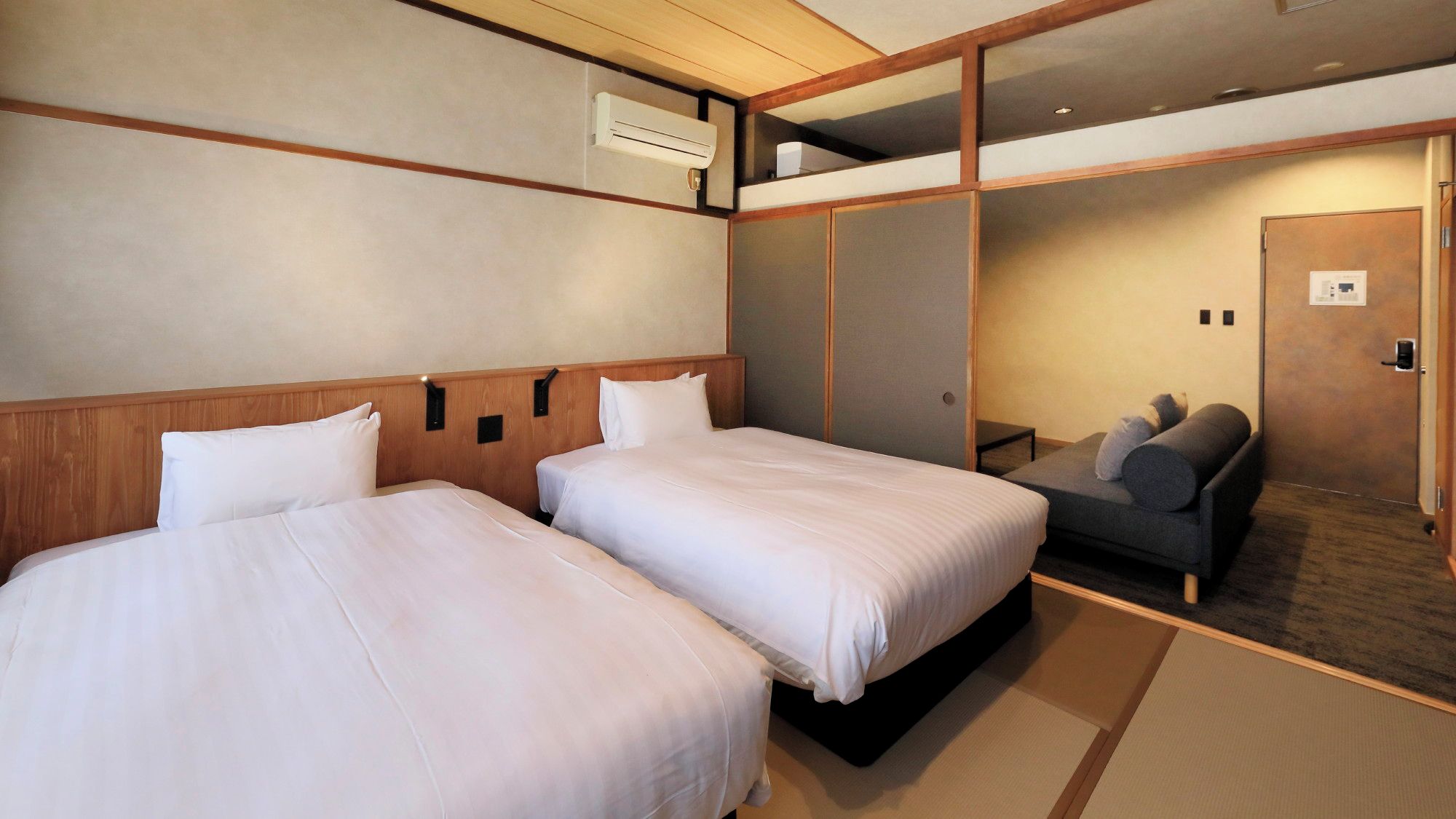 Habitación de hotel con dos camas, un sofá y puerta corredera que da a un balcón.
