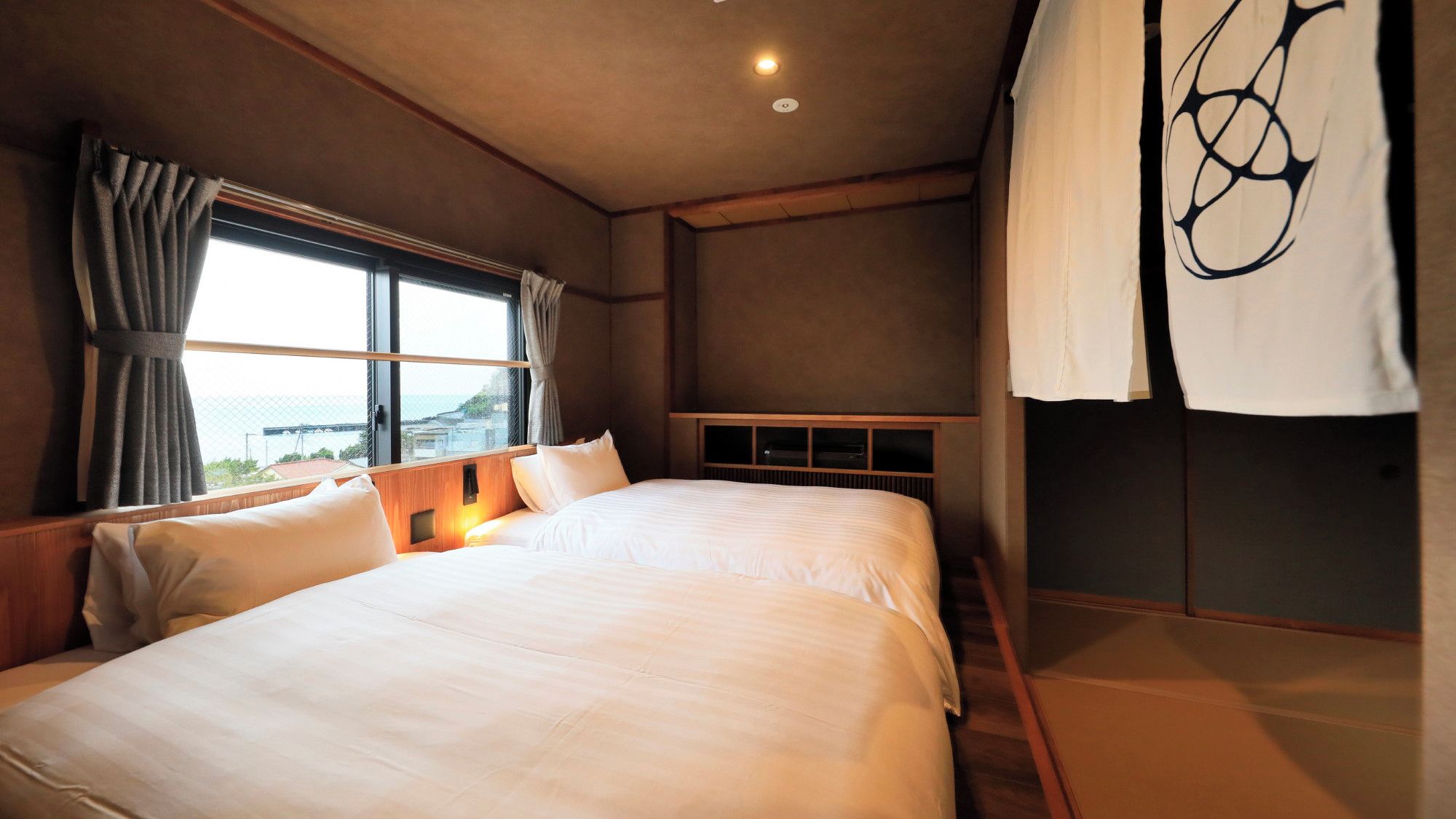 A hotel room with a large bed, a window with curtains, a view of the sea, and a wall with a decorative design.