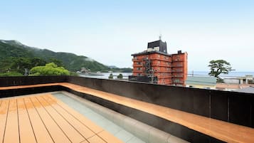 A rooftop terrace with a wooden deck and a view of a red building and mountains.