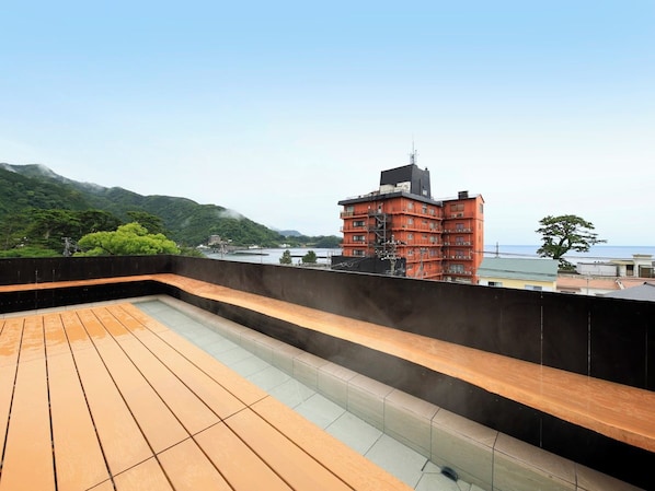 A rooftop terrace with a wooden deck and a view of a red building and mountains.
