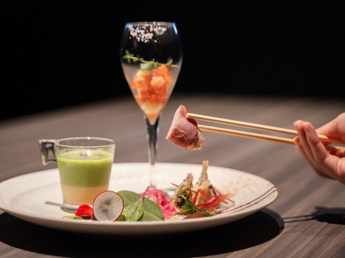A plate with a green drink, a glass with a garnish, and a dish with food and chopsticks.