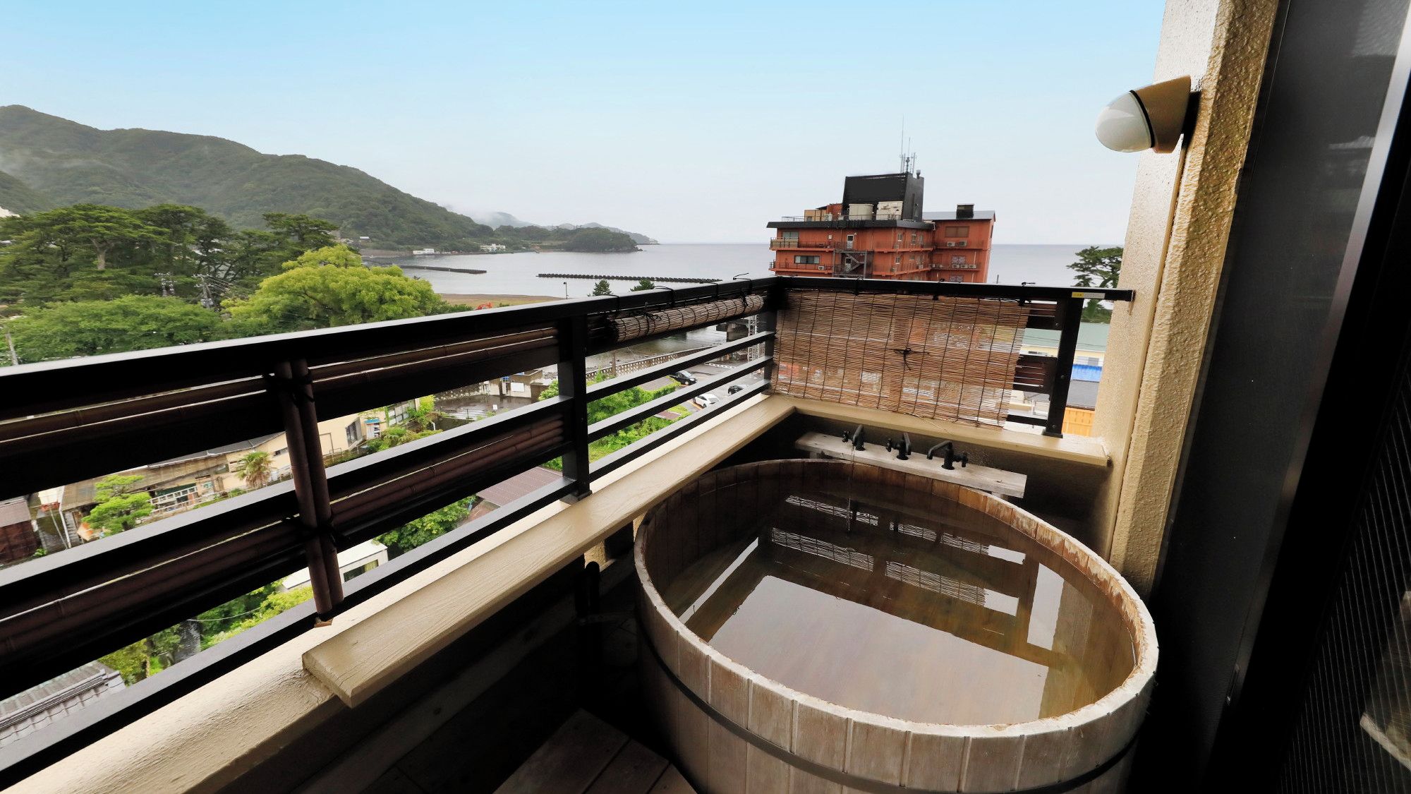 Un balcón con un jacuzzi de madera, vista a un cuerpo de agua y una montaña distante.