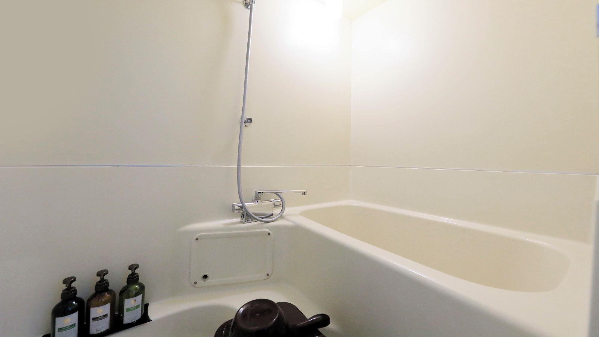 Ein Badezimmer mit einer Badewanne, einer Duschbrause und zwei Flaschen Flüssigseife auf dem Boden.