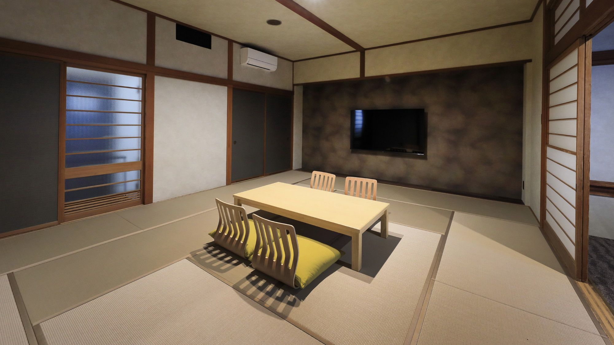 A traditional Japanese-style room with tatami flooring, a low table, and a TV mounted on the wall.