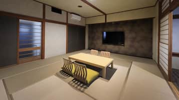 A traditional Japanese-style room with tatami flooring, a low table, and a TV mounted on the wall.