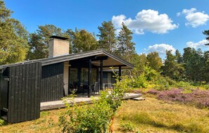 Ein modernes Blockhaus mit überdachter Veranda, eingebettet in eine natürliche Landschaft.