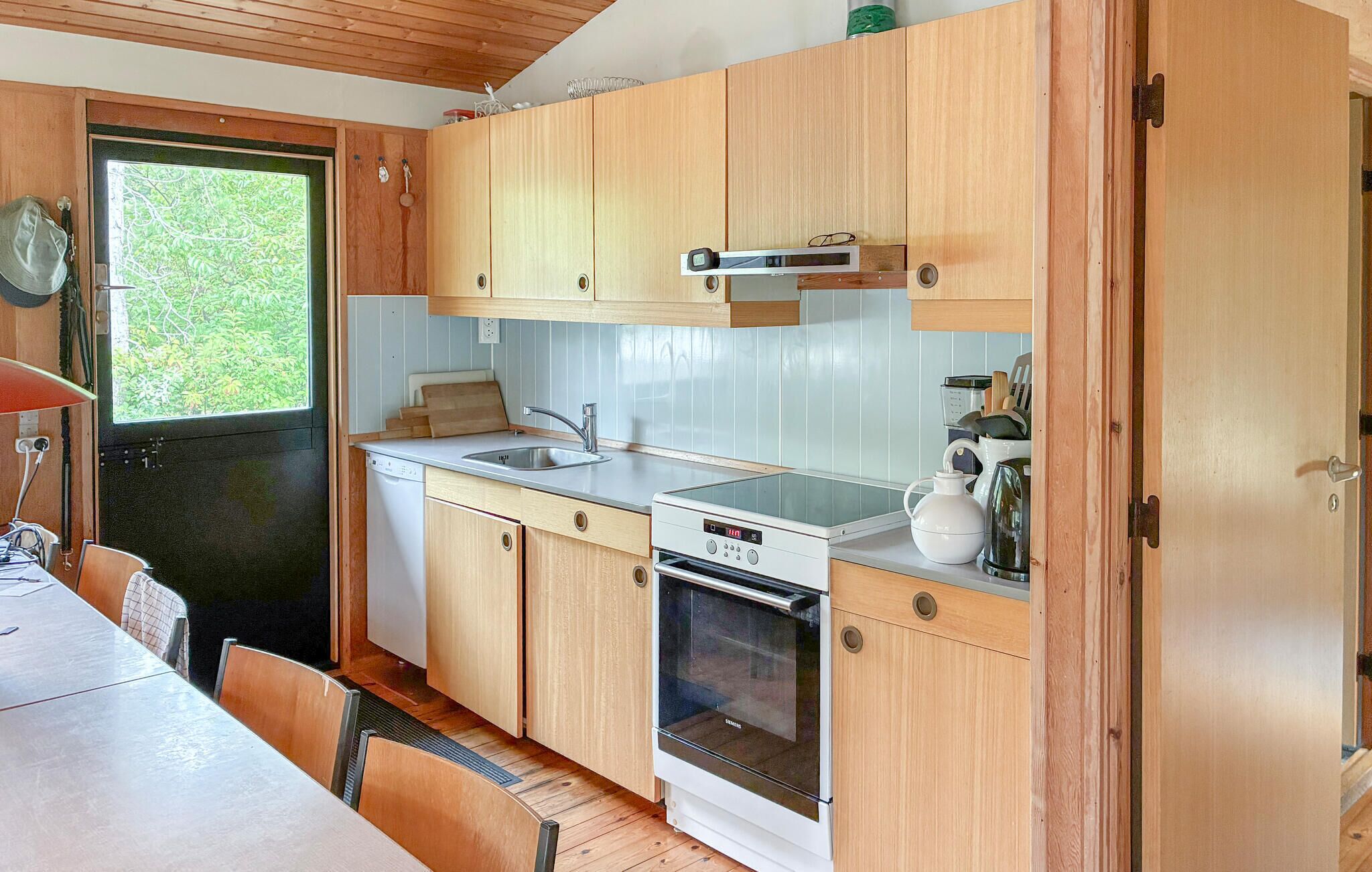 Une cuisine compacte avec des meubles en bois, un évier, un lave-vaisselle, un four et une fenêtre donnant sur un espace verdoyant.