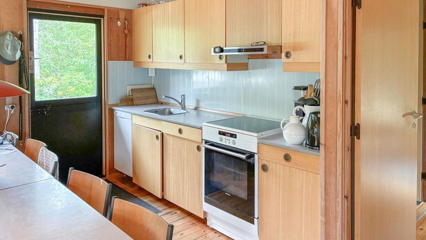 Uma cozinha compacta com armários de madeira, pia, lava-louças, forno e uma janela com vista para o verde.