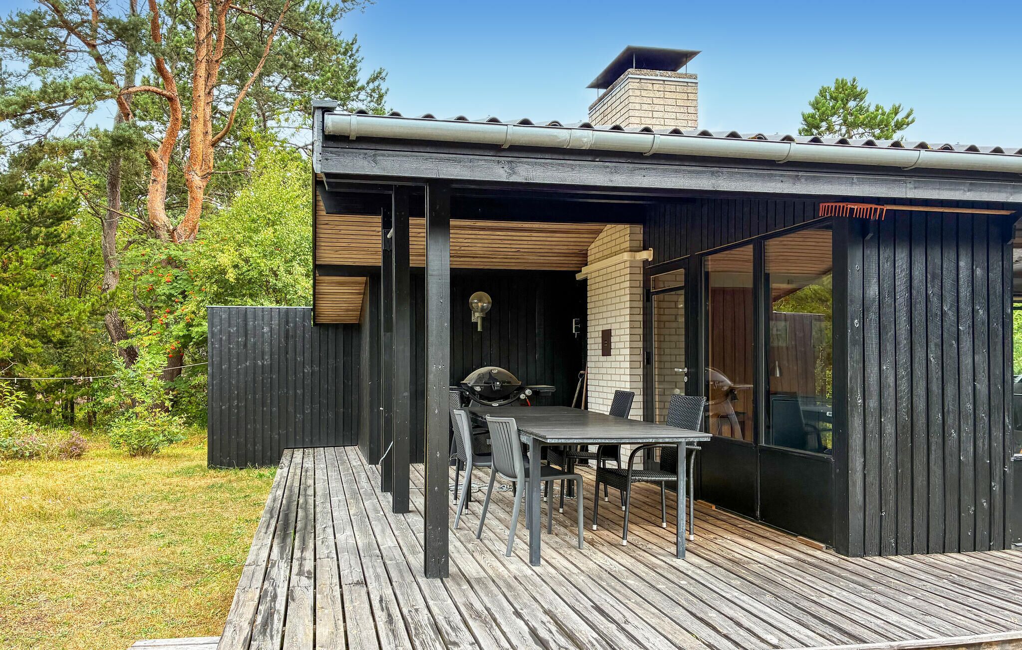 A wooden deck with a table and chairs, a grill, and a brick chimney.