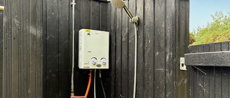 A portable water heater mounted on a wooden fence with a hose and showerhead attached.