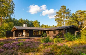 A modern cabin with a large deck, surrounded by dense forest and purple heather. - Stunning home in Højby with WiFi (Højby)
