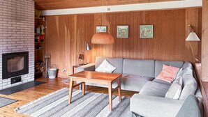 Uma sala de estar com lareira, paredes de madeira, um sofá cinza, uma mesa de centro de madeira e um tapete listrado.