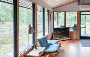A modern interior with large windows, a wooden floor, a seating area with a blue cushion, and a table with binoculars and a remote control. - Stunning home in Højby with WiFi (Højby)