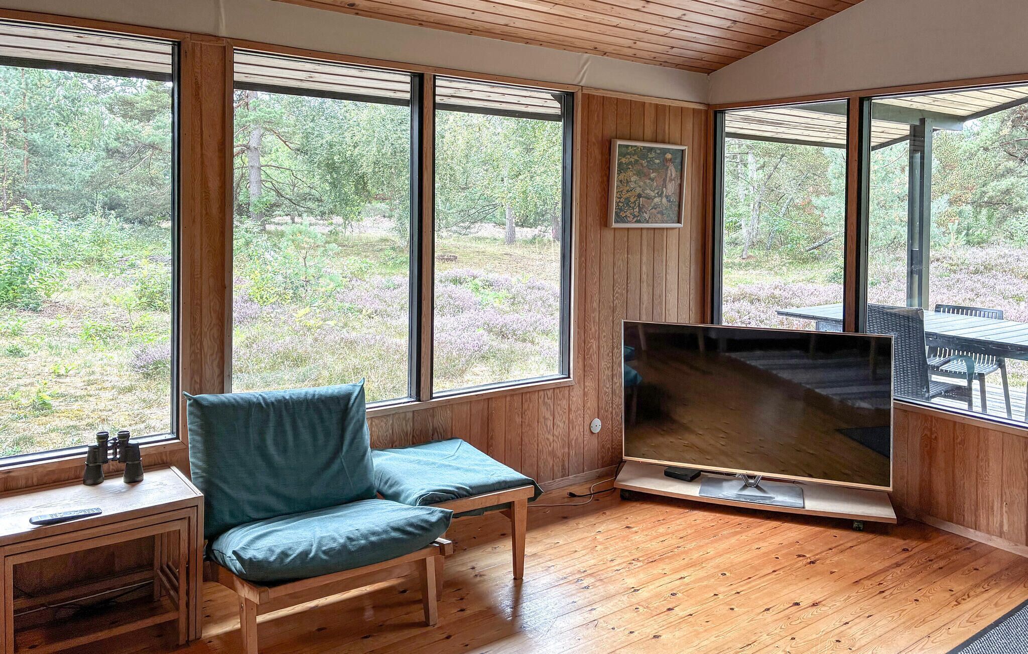 A room with large windows, a television, and a wooden table with a chair.