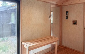 Eine Holzbänk in einem Raum mit einem großen Fenster, einem Wandthermostat und einem kleinen dekorativen Gegenstand.