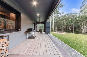A covered outdoor area with a grill, seating, and a view of the surrounding forest.