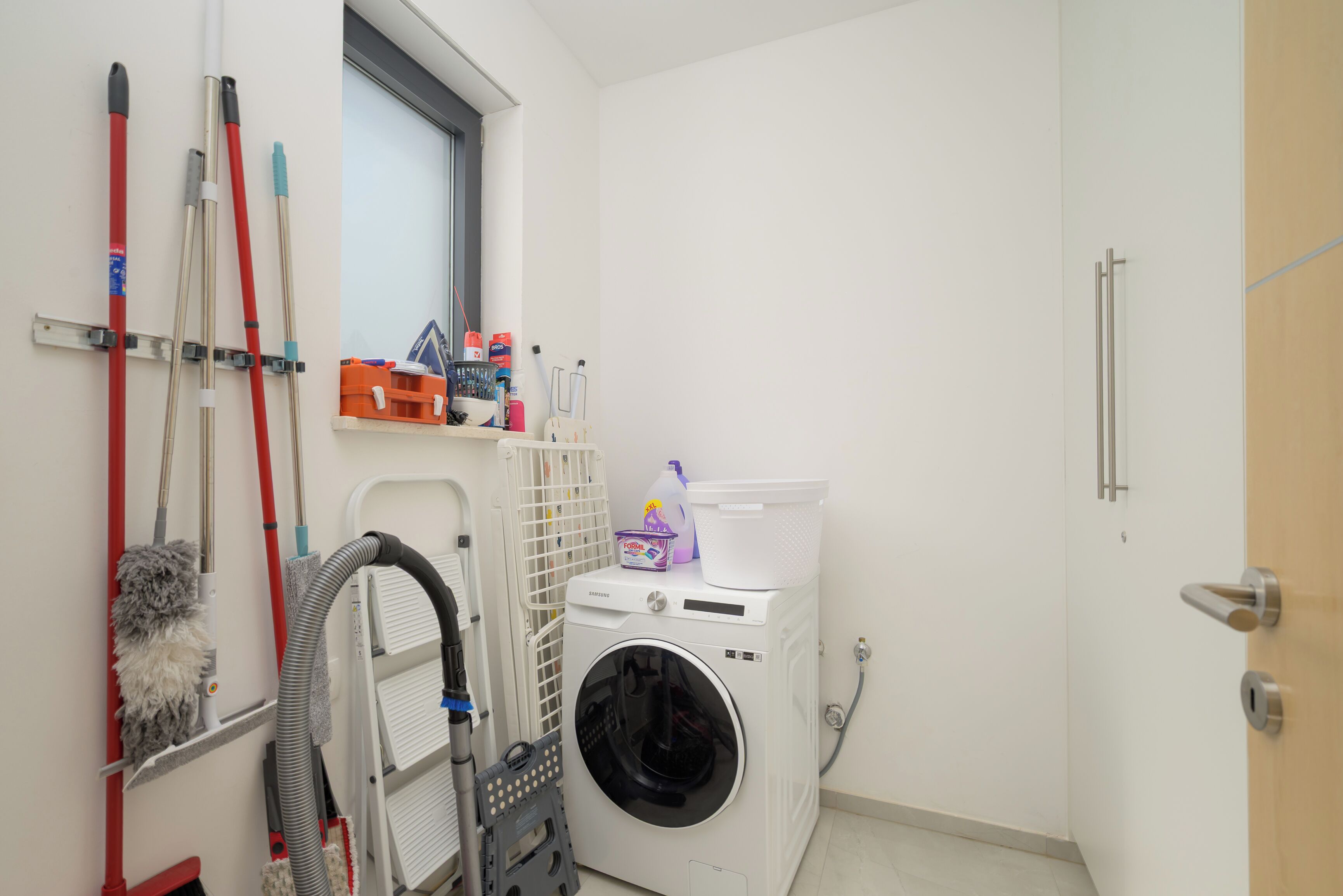 A laundry room with a washing machine, mops, and cleaning supplies.