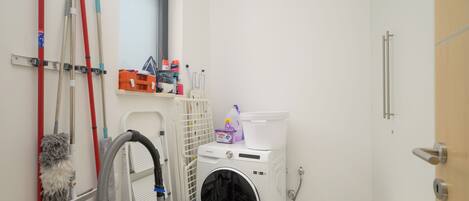 A laundry room with a washing machine, mops, and cleaning supplies.