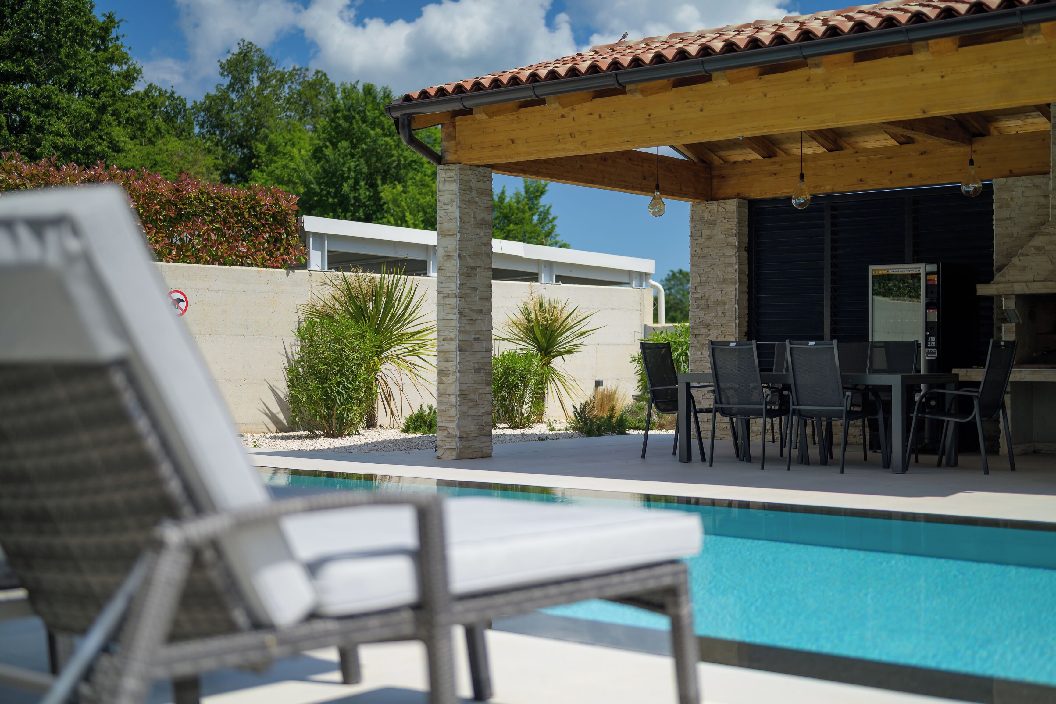 Un espace aménagé au bord de la piscine, avec des chaises longues, une pergola et un coin repas.