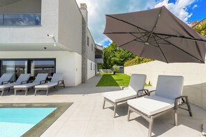 Ein moderner Poolbereich im Freien mit Liegestühlen und einem großen Sonnenschirm.