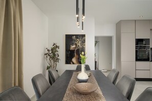 Ein moderner Essbereich mit einem langen Tisch, Stühlen, einer Blumenvase und einem Bild an der Wand.