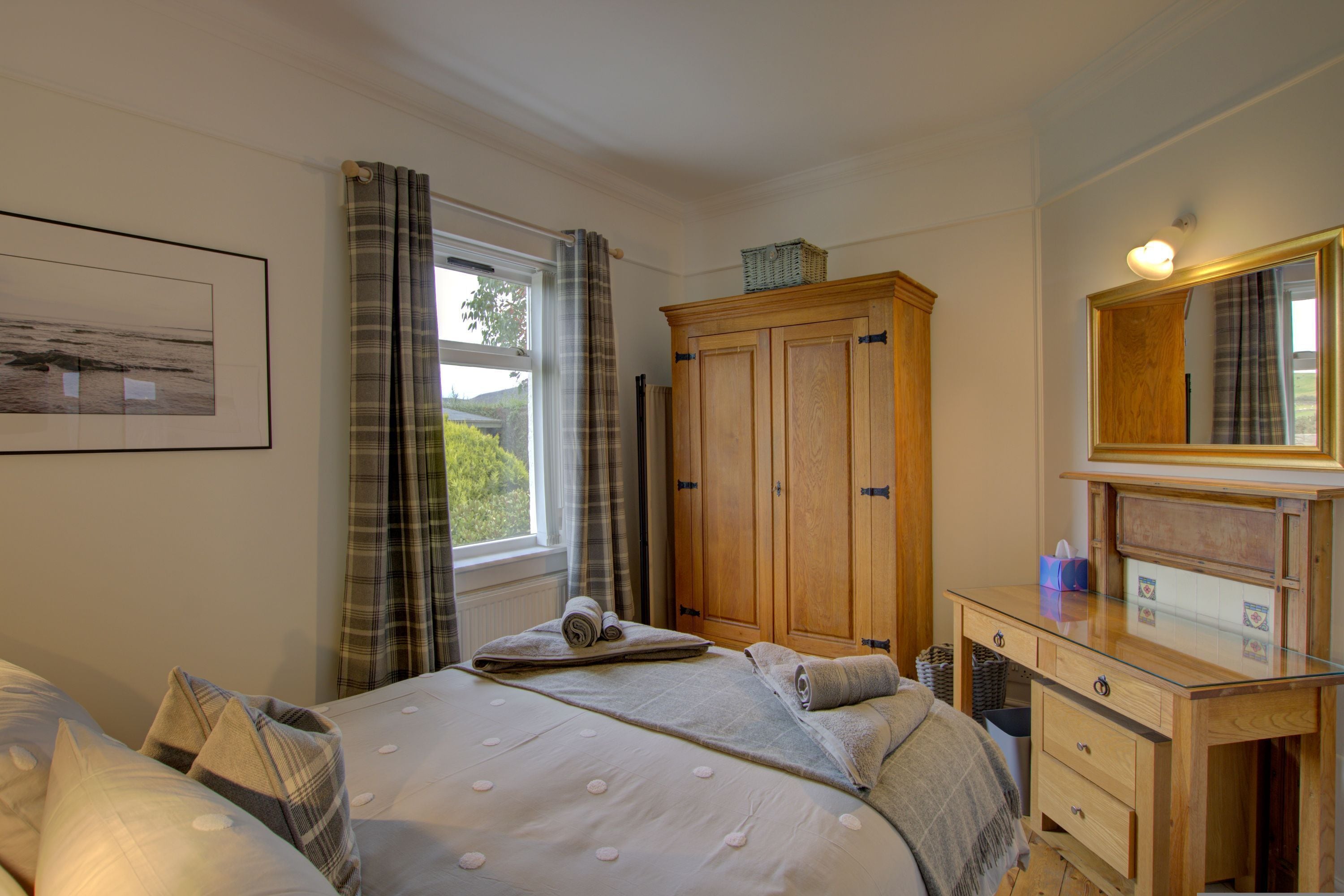 A bedroom with a bed, a dresser, a mirror, and a window with curtains.