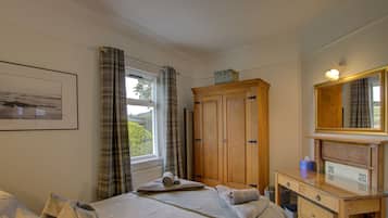 A bedroom with a bed, a dresser, a mirror, and a window with curtains.