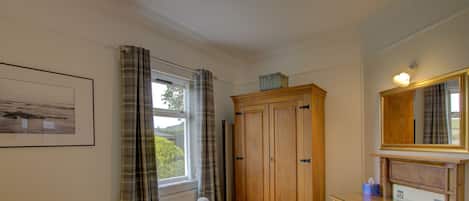 Une chambre à coucher avec un lit, une commode, un miroir et une fenêtre avec des rideaux.