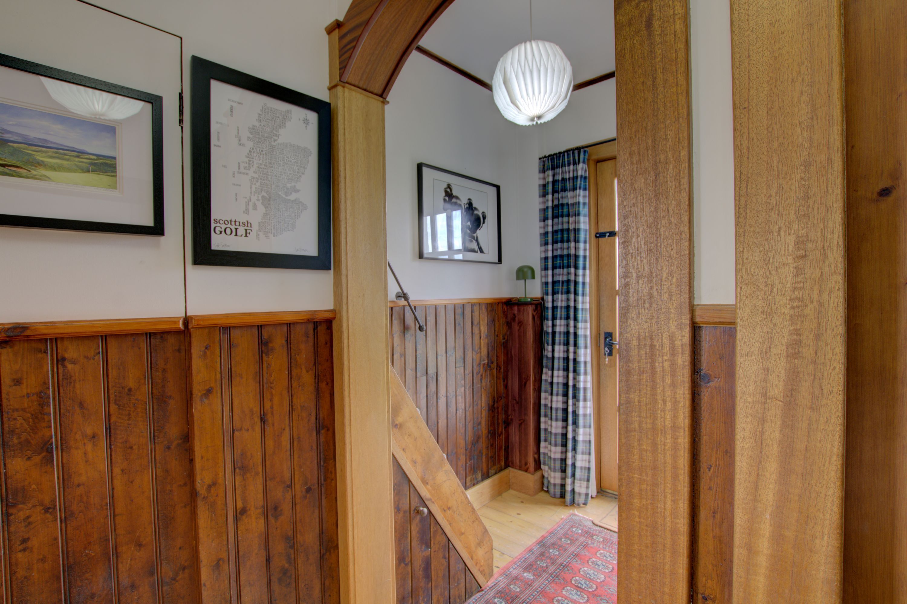 A wooden staircase leading to a room with a plaid curtain, a framed map, and a hanging light fixture.