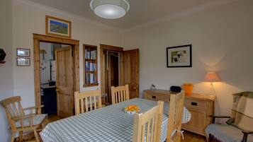 A dining area with a checkered tablecloth, wooden chairs, a wooden cabinet, and a lamp.