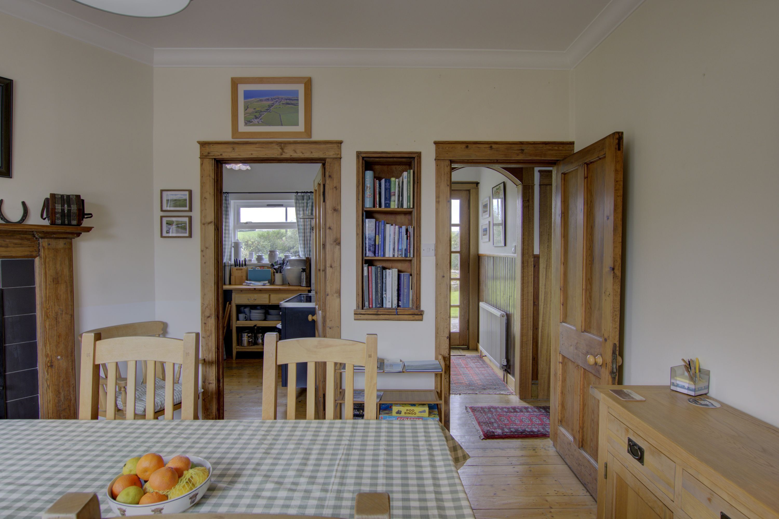 Un coin repas avec une nappe à carreaux, des chaises en bois, un panier de fruits et une bibliothèque remplie de livres.
