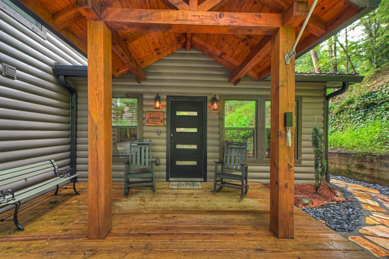 A log cabin with a porch, two rocking chairs, and a bench.