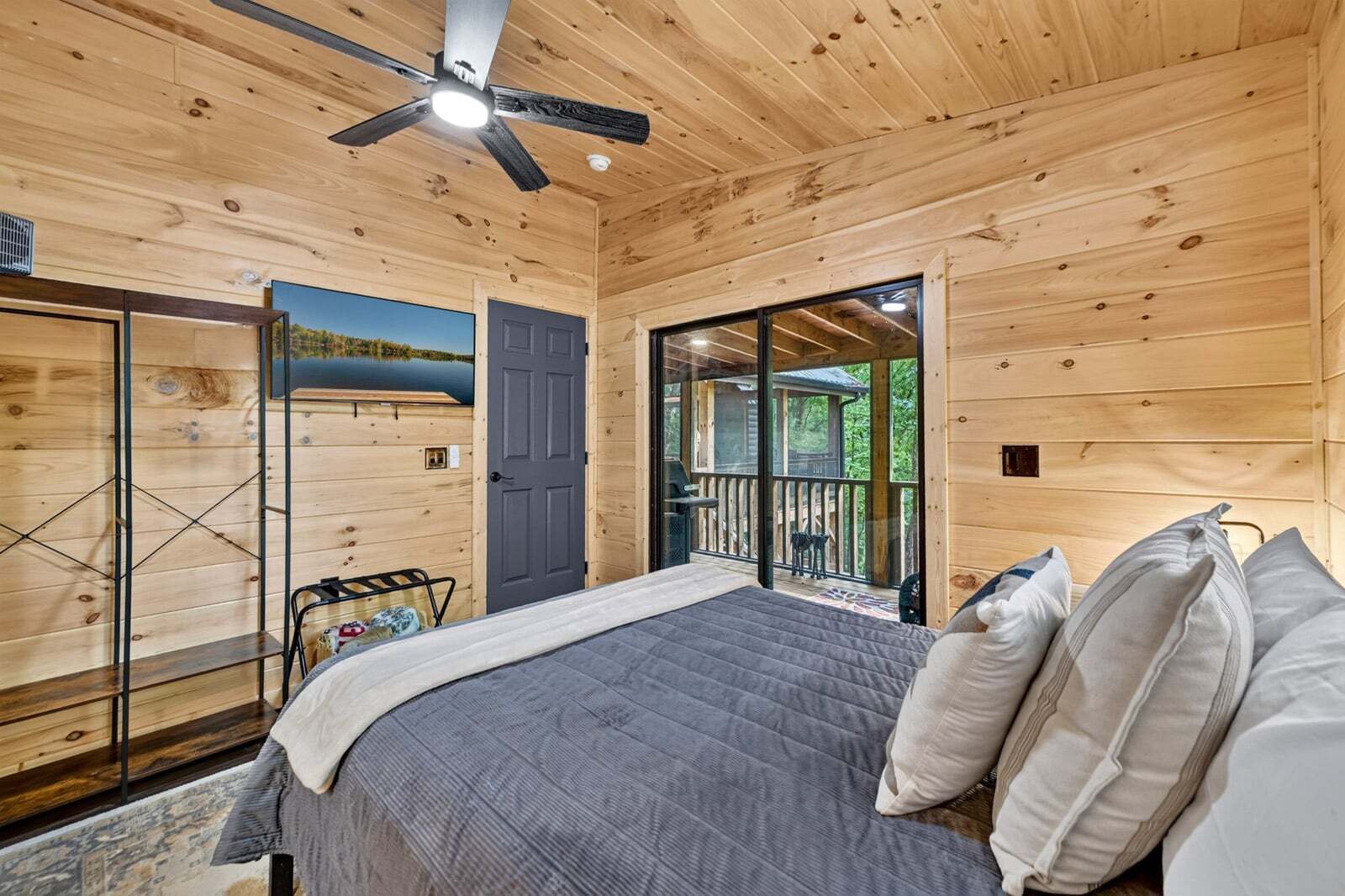 A wooden cabin bedroom with a bed, pillows, a ceiling fan, and a view of the outdoors.