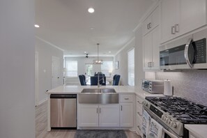 A modern kitchen with white cabinetry, stainless steel appliances, and a dining area with blue chairs. - Cozy Newer Home Close to Lake Conroe, Pool, Golf Course, Tennis & Country Club! (Montgomery)